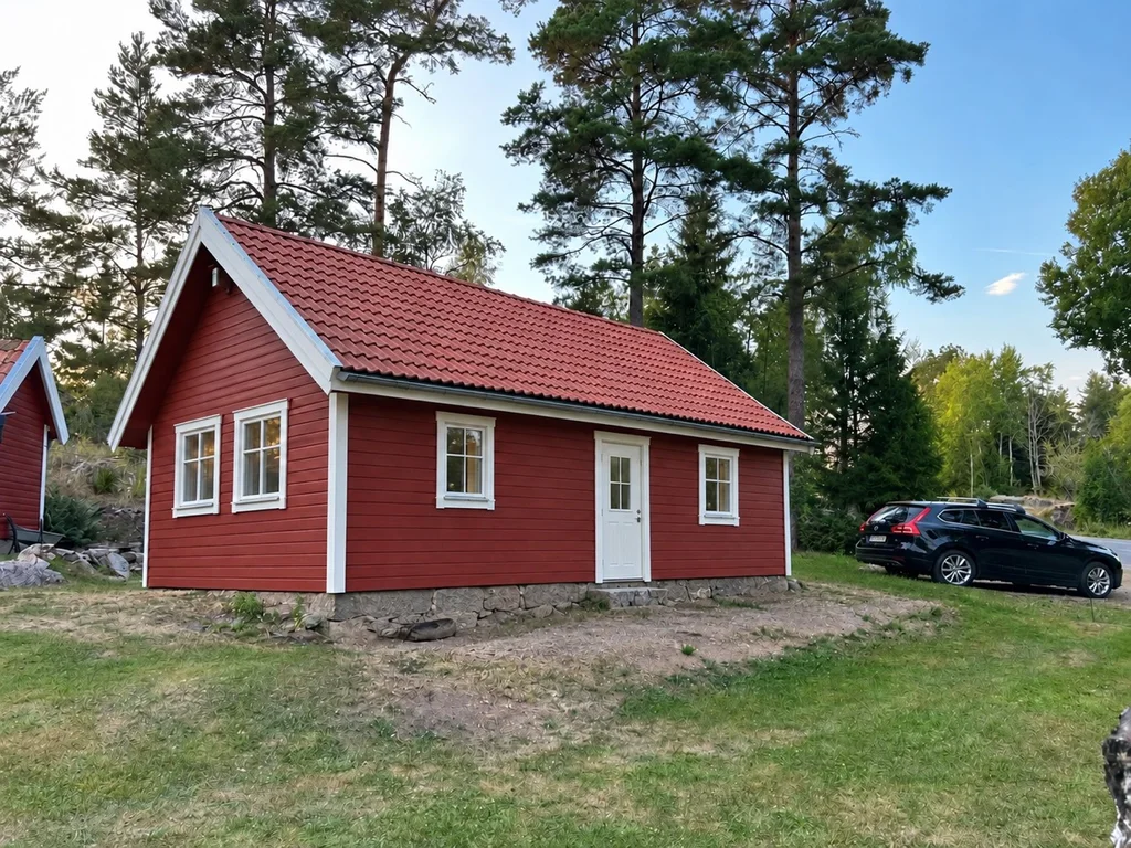 Bro Solviks röda semesterstuga med vita fönster och vit dörr bland träden